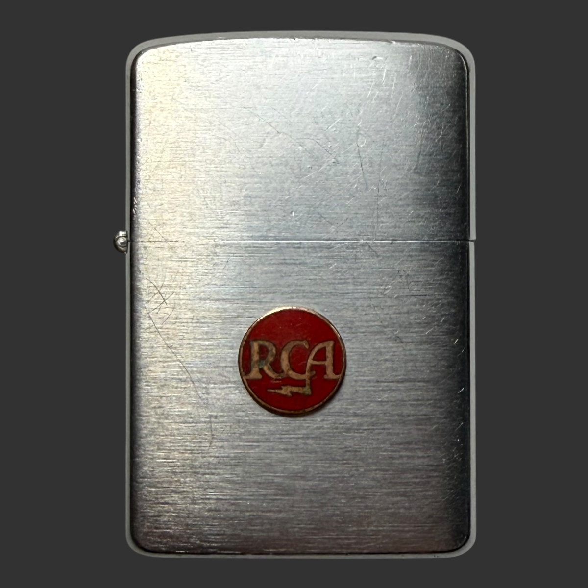 1957 vintage Zippo lighter with factory-applied red enamel RCA advertising emblem, brushed chrome finish showing natural patina and wear