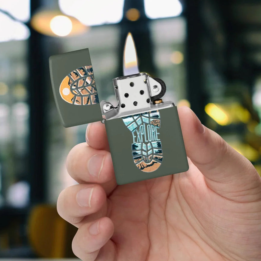Green Matte Step Out Zippo lighter with mountain landscape inside a footprint and “Explore” inscription in hand.